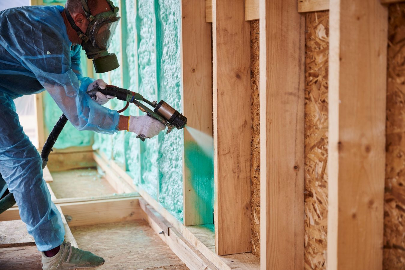 Worker spraying polyurethane foam for insulating wooden frame house. Male builder insulating wooden frame house. Man worker spraying polyurethane foam inside of future cottage, using plural component gun. Construction and insulation concept.